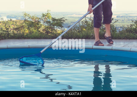 L'uomo la pulizia piscina di caduta foglie con rete di pulizia al mattino. Foto Stock