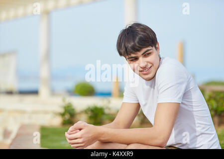 Ritratto di giovane uomo seduto con le mani giunte sorridente Foto Stock
