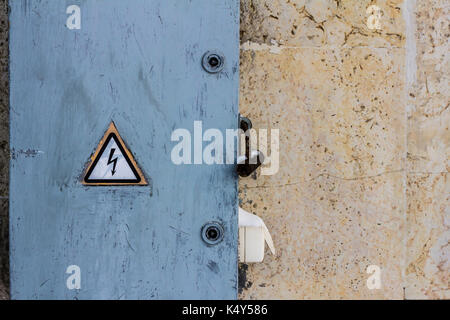 Pericolo di scossa elettrica segno posto su un blocco di potenza elettrico cruscotto su un graffiato parete dipinta Foto Stock