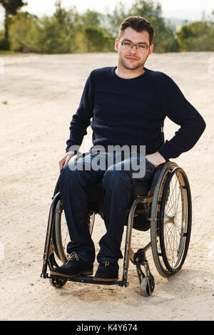 Giovane uomo disabili in carrozzella sorriso al di fuori. Foto Stock