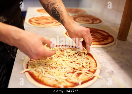 Cuocere aggiungendo il formaggio grattugiato per la pizza in pizzeria Foto Stock