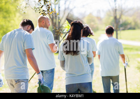 Il volontariato, carità, le persone e il concetto di ecologia - gruppo di volontari felice con le piantine di alberi e attrezzi da giardino passeggiate nel parco Foto Stock