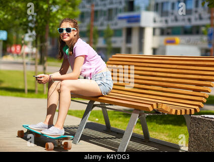 Felice ragazza adolescente con cuffie e longboard Foto Stock