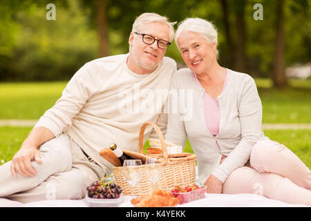 Vecchiaia, vacanze, tempo libero e concetto di persone - felice coppia senior con Cesto picnic seduti su una coperta al summer park Foto Stock