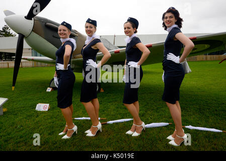 Femmine al Goodwood Revival 2017 in stile hostess d'epoca. Evento retrò in cattive condizioni atmosferiche. Con Spitfire aereo Foto Stock