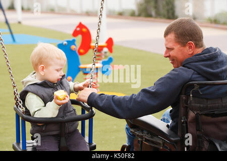 Padre disabili gioca con il suo piccolo figlio sul parco giochi Foto Stock