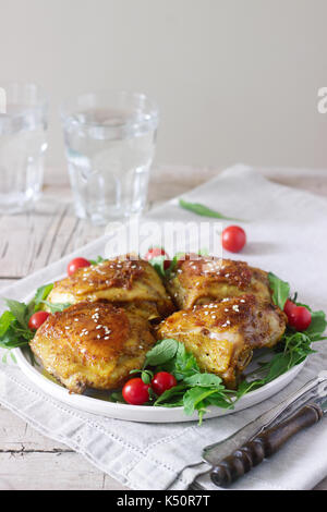 Cotto al forno cosce di pollo con guarnite di foglie di rucola e pomodori. stile rustico, il fuoco selettivo. Foto Stock