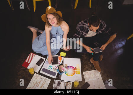 Angolo alto ritratto di sorridere giovani designer femmina seduta dal collega di sesso maschile con fogli sul pavimento nel coffee shop Foto Stock