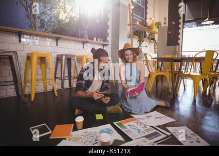 Giovani di sesso femminile che mostra professionale latteria alla collega di sesso maschile seduto sul pavimento nel coffee shop Foto Stock