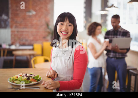 Ritratto di giovane sorridente donna seduta con insalata fresca a tavola in coffee shop Foto Stock