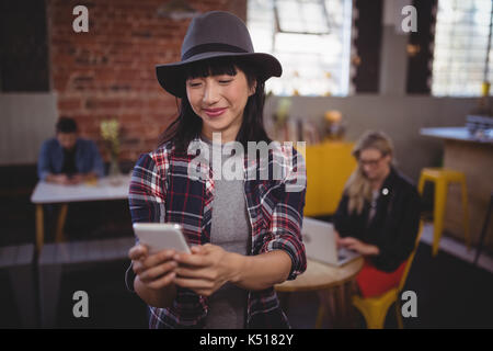 Sorridente giovane donna attraente usando il cellulare mentre in piedi presso la caffetteria Foto Stock