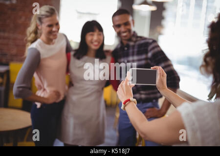 Immagine ritagliata della donna fotografa amici dallo smartphone al coffee shop Foto Stock