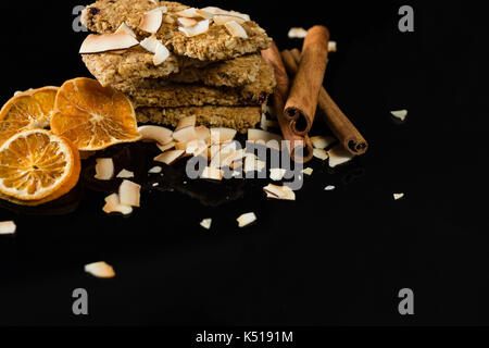 Granola bar con noce di cocco essiccata, bastoncini di cannella e fettine di arancio su sfondo nero Foto Stock