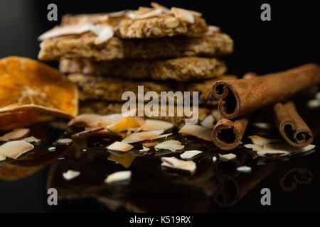 Granola bar con noce di cocco essiccata, bastoncini di cannella e fettine di arancio su sfondo nero Foto Stock