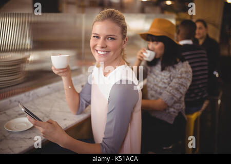 Ritratto di sorridente giovane donna di bere il caffè mentre si utilizza il telefono cellulare al contatore nel coffee shop Foto Stock