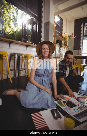 Ritratto di giovane sorridente femmina seduta professionale con il collega di sesso maschile sul pavimento nel coffee shop Foto Stock