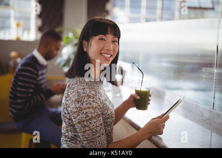 Ritratto di sorridente giovane donna azienda bere e tablet presso il cafe Foto Stock