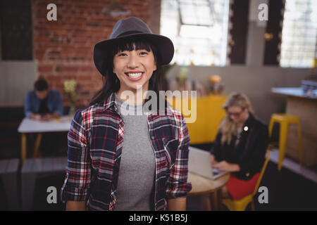 Ritratto di sorridente giovane donna indossa hat permanente al coffee shop Foto Stock