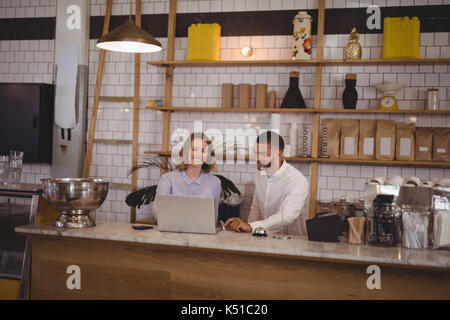 Giovane maschio proprietario e cameriera utilizzando computer portatile mentre è seduto al banco in coffee shop Foto Stock