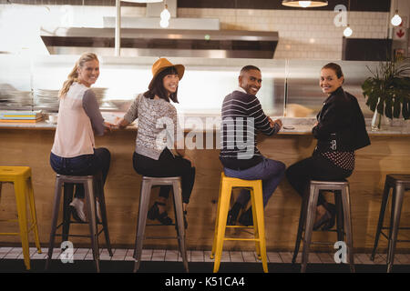 Vista posteriore del ritratto di sorridere giovani amici seduti su sgabelli a contatore nel coffee shop Foto Stock