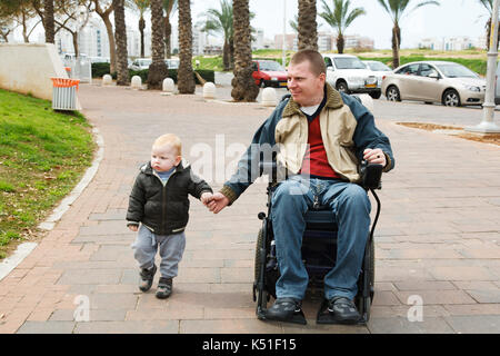Papà passeggiate in una sedia a rotelle con un giovane figlio Foto Stock