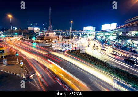 Il traffico nella rotonda che circonda il monumento della vittoria di notte a Bangkok, in Thailandia Foto Stock