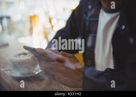 La sezione centrale dell'uomo con caffè utilizzando phone visto attraverso il vetro in cafe Foto Stock