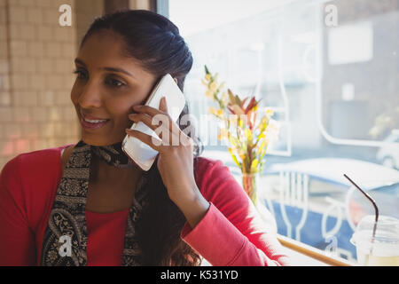 Giovane donna che guarda lontano mentre si parla al telefono cellulare in cafe Foto Stock