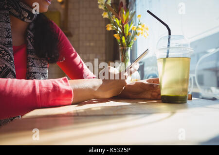 La sezione centrale della donna con drink usando il telefono al davanzale in cafe Foto Stock