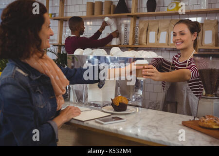 Giovani femmine proprietario che serve caffè al cliente presso il cafe Foto Stock