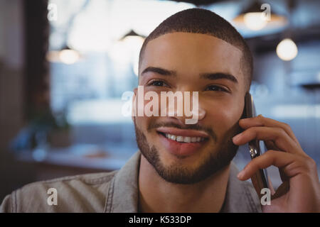 Close-up del giovane uomo che parla al telefono cellulare in cafe Foto Stock