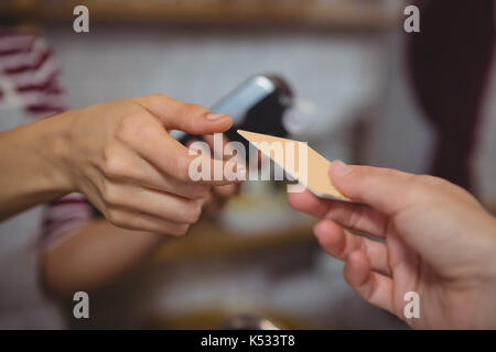 Ritagliate la mano del cliente che effettua il pagamento al proprietario di sesso femminile presso il cafe Foto Stock