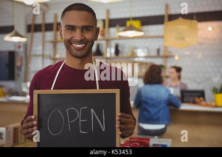 Ritratto del proprietario sorridente con open firmare in piedi in cafe Foto Stock