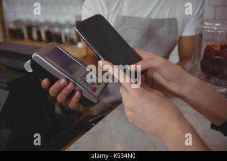 Ritagliate la mano del cliente che effettua il pagamento senza contatto con cameriere tenendo il lettore di carte di credito in cafe Foto Stock