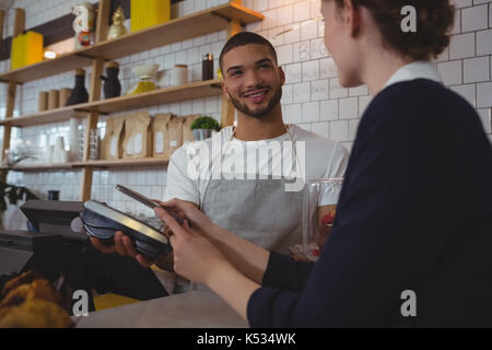 Giovane cameriere che mostra un lettore di carte di credito a femmina proprietario in cafe Foto Stock