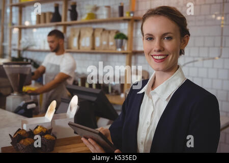 Ritratto di donna sorridente proprietario utilizzando tavoletta digitale con cameriere che lavorano in cafe Foto Stock