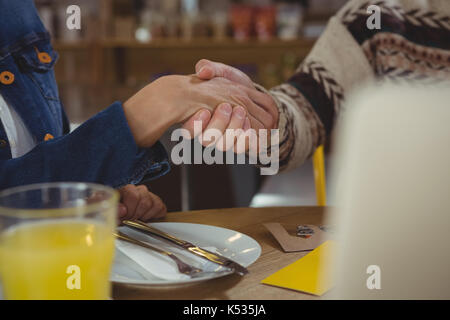 Immagine ritagliata di uomini di affari che stringono le mani a tavola in cafe Foto Stock