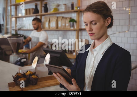 Proprietario femmina con tavoletta digitale con cameriere che lavorano in cafe Foto Stock