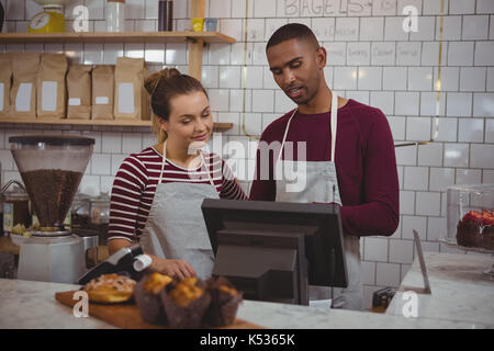 Giovani proprietari utilizzando un registratore di cassa mentre in piedi in cafe Foto Stock