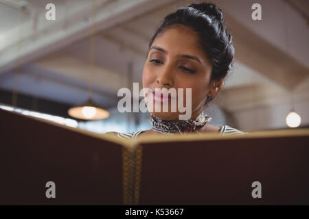 Giovane donna menu di lettura in cafe Foto Stock