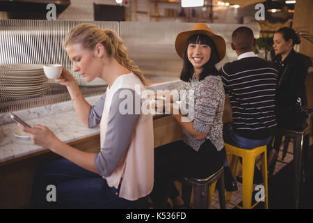 Ritratto di giovane sorridente donna seduta in mezzo agli amici a contatore nel coffee shop Foto Stock