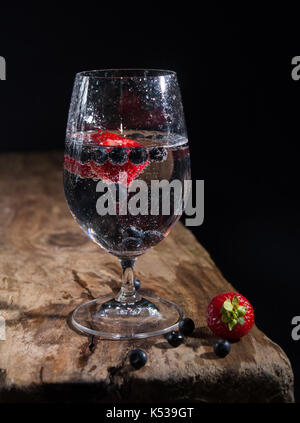 Bicchiere di acqua frizzante con fragole fresche e mirtilli neri Foto Stock