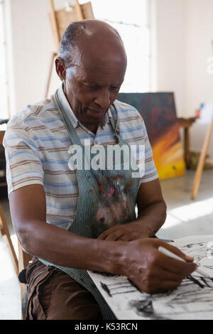 Senior uomo pittura su carta mentre è seduto a tavola in classe d'arte Foto Stock