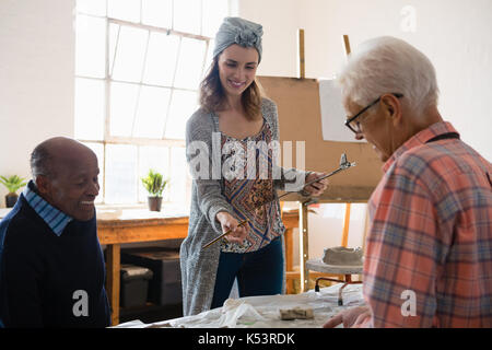 Donna sorridente holding appunti mentre parla con artisti maschi in classe d'arte Foto Stock