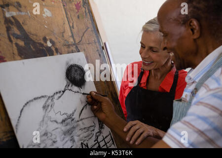 Donna senior di aiutare l uomo mentre la pittura su carta in classe d'arte Foto Stock