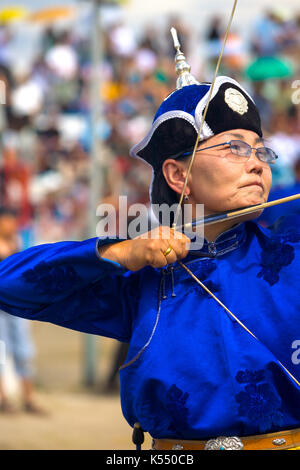 Ulaanbaatar, in Mongolia - giugno 11, 2007: femmina archer in blu abiti tradizionali tirando indietro la sua bowstring e concentrando al naadam festival a Foto Stock