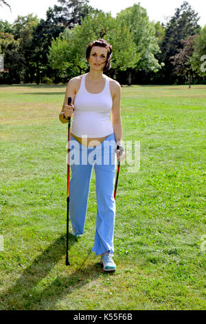 Donna incinta in estate facendo nordic walking Foto Stock