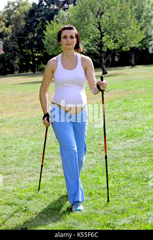 Donna incinta in estate facendo nordic walking Foto Stock