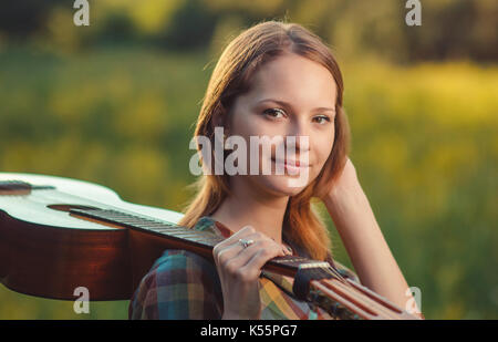 Ritratto di un musicista giovane donna in plaid shirt con un acustica chitarra in legno sulla spalla su colorfull estate sfondo. Foto Stock