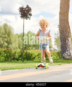 Bambina a cavallo di uno scooter al parco Foto Stock